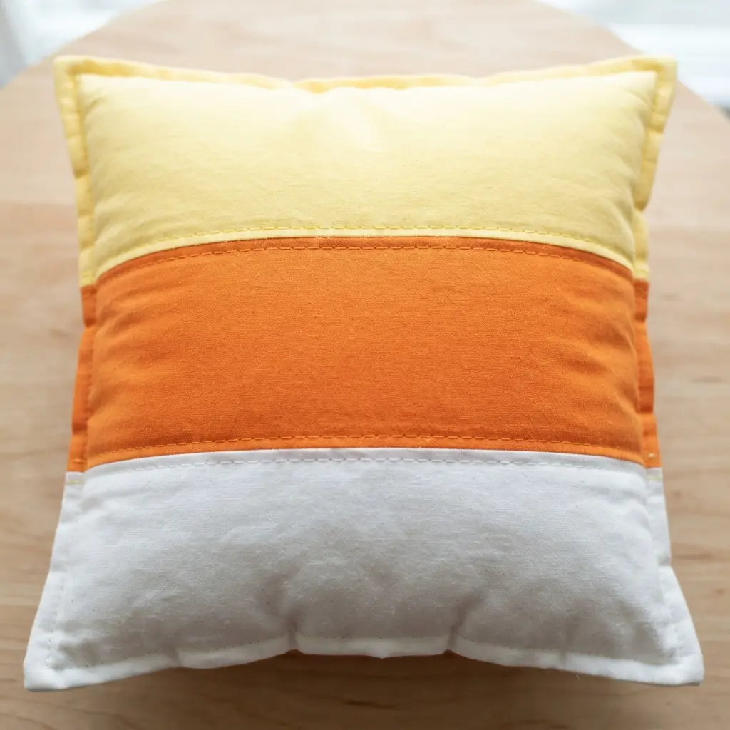 A plush throw pillow with a front panel made from striped yellow, orange, and white fabric.