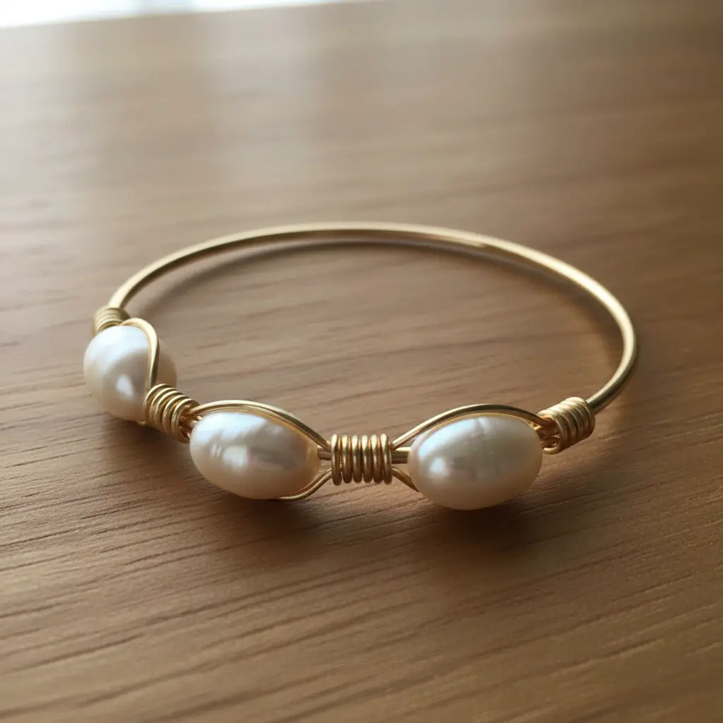 A close-up view of a rigid gold wire bangle with three smooth, cream-colored pearls securely wrapped in place.
