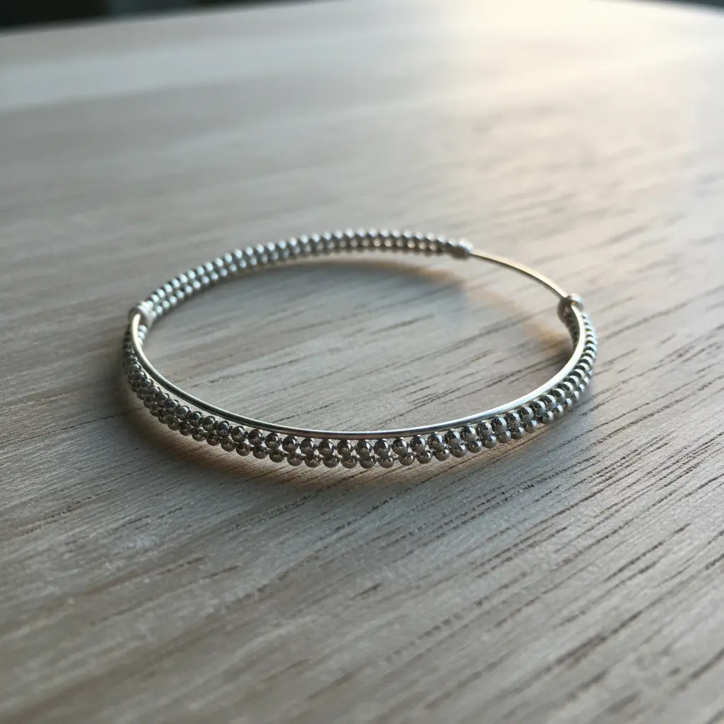 A thin, silver wire bangle featuring a subtle pattern created by closely strung metallic silver seed beads.