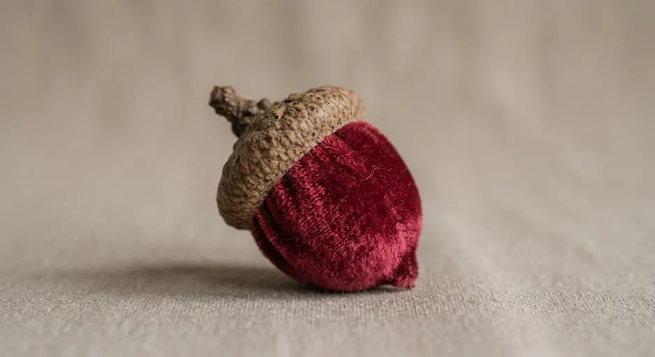 Three acorns wrapped in rich velvet fabric in emerald and wine colors, displayed on a marble surface.