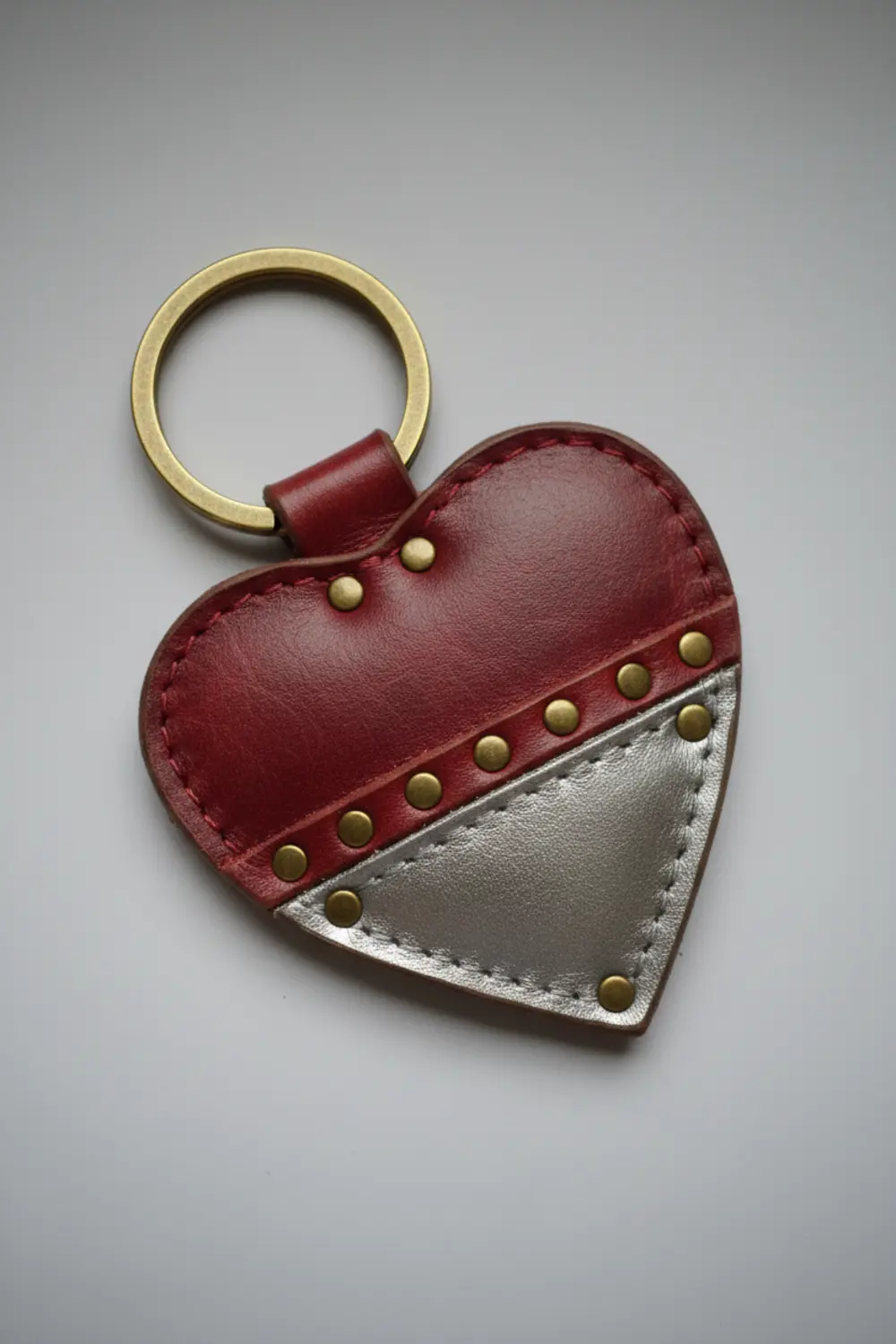 A heart-shaped keychain made from pink and red faux leather layers, secured together with small silver rivets.