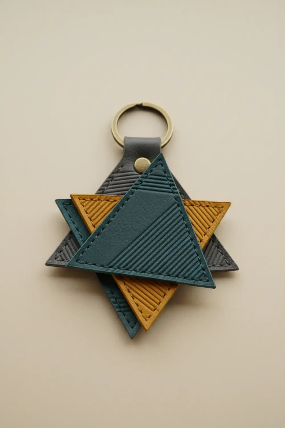 A geometric triangle keychain made from two layers of black faux leather, joined with precise white stitching along the edges.