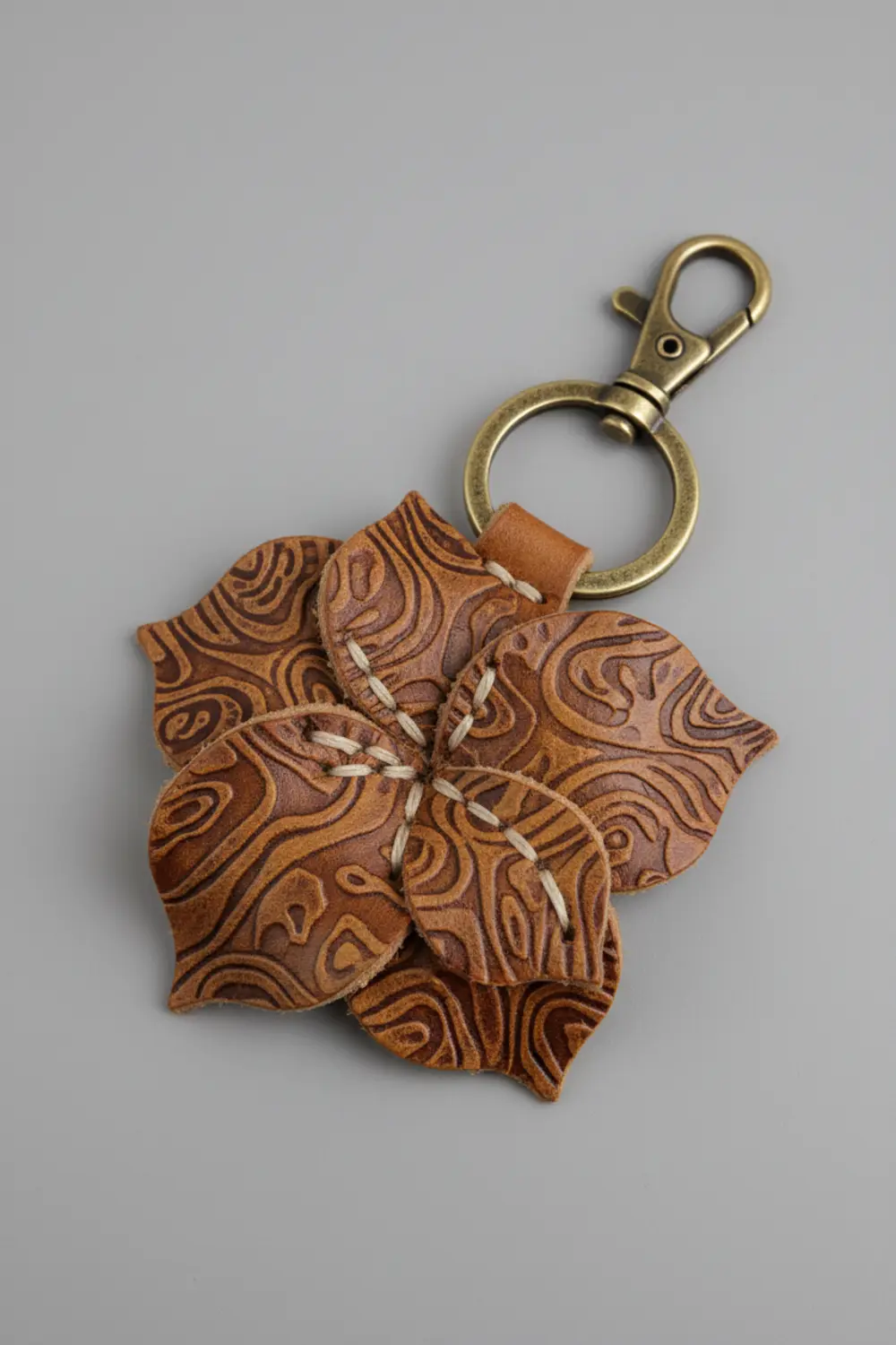 A brown faux leather keychain cut into a flower shape, showcasing a deep, embossed texture on each petal.