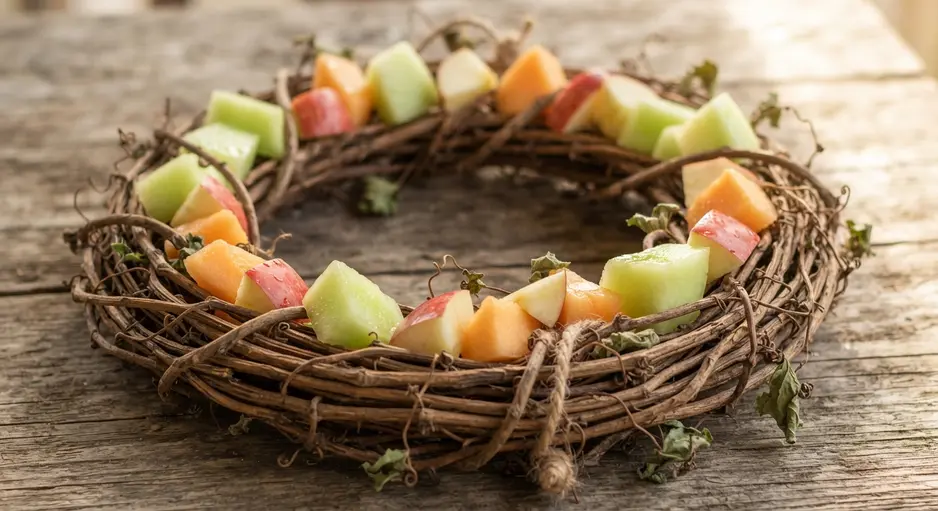 A rustic wreath of dried vines holding chunks of melon and apple, hanging on a garden gate.