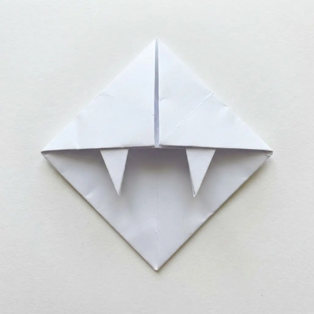 A white origami paper corner bookmark designed to look like a pair of sharp vampire fangs.