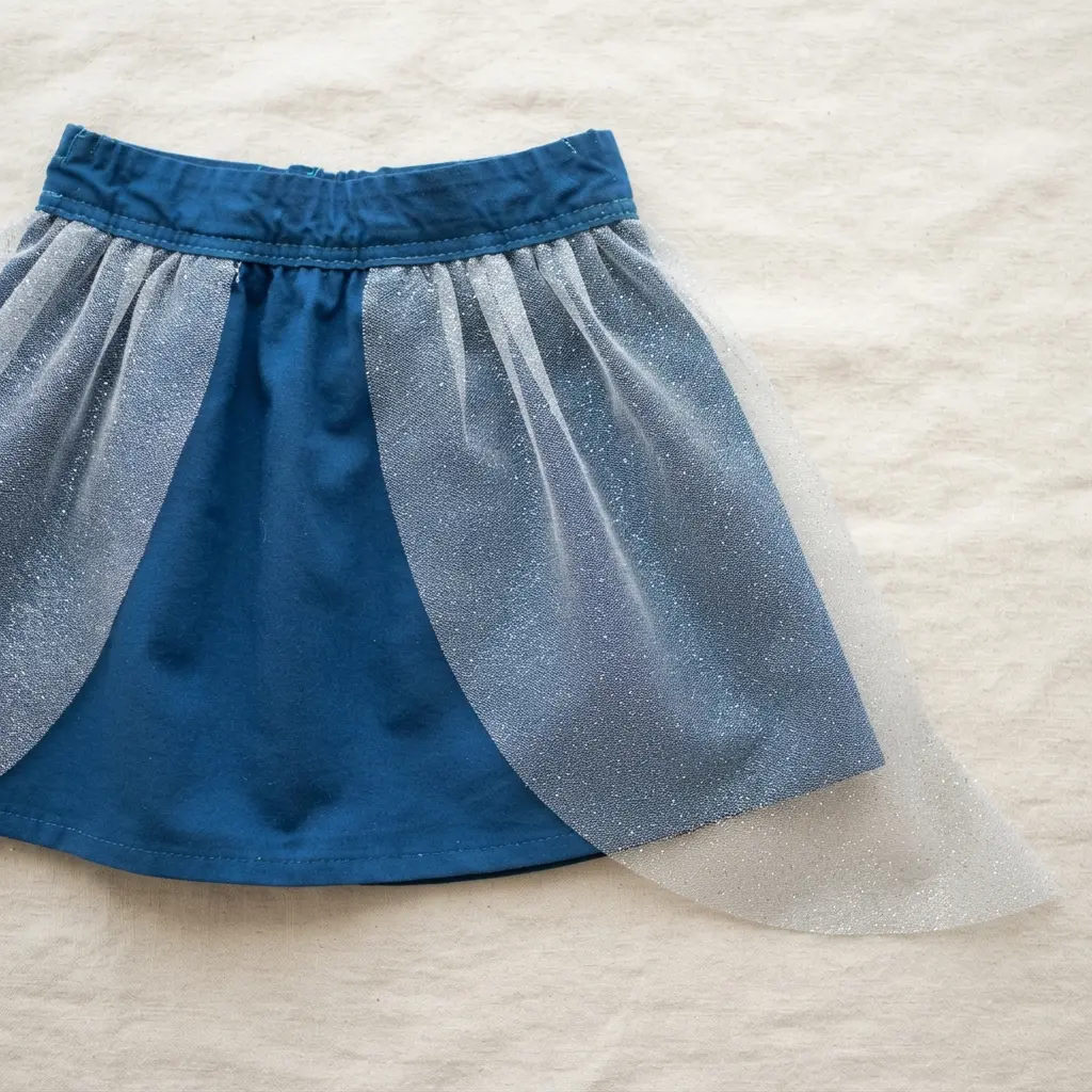 A skirt with a solid colored base layer and a sheer, glittery mesh overlay cut into a fin shape at the back.