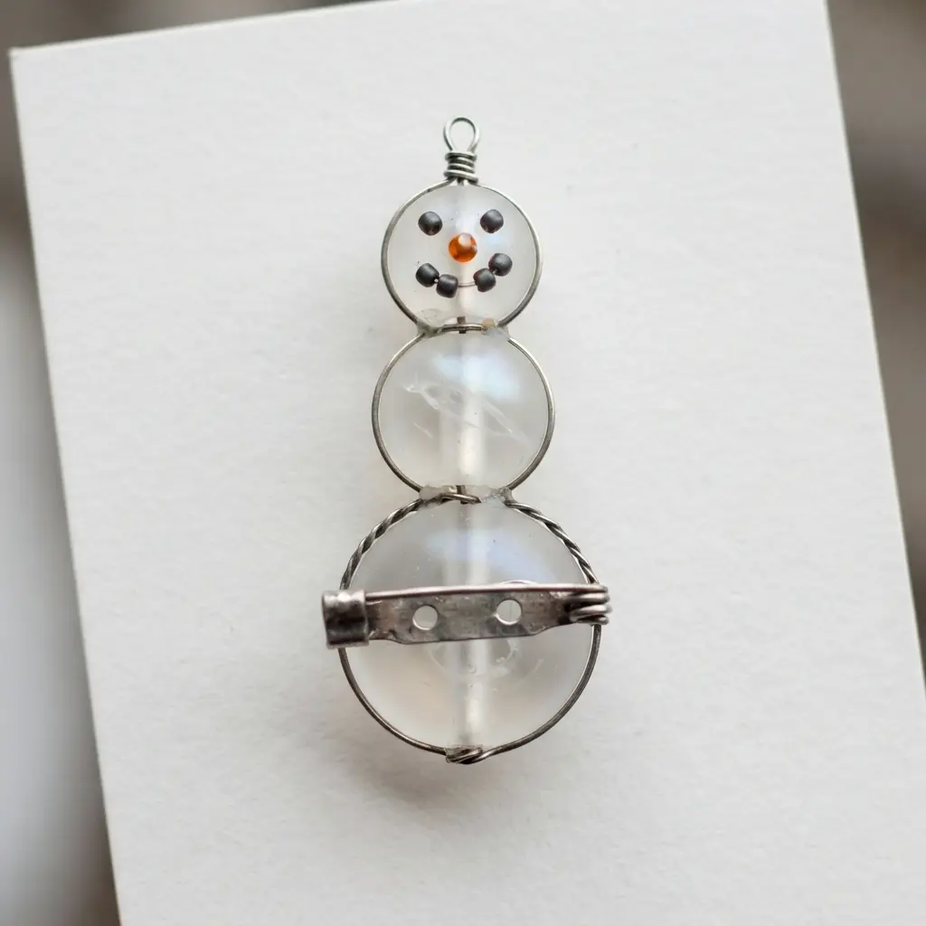A snowman brooch constructed from three white glass pearls stacked vertically and fastened with a silver pin back.