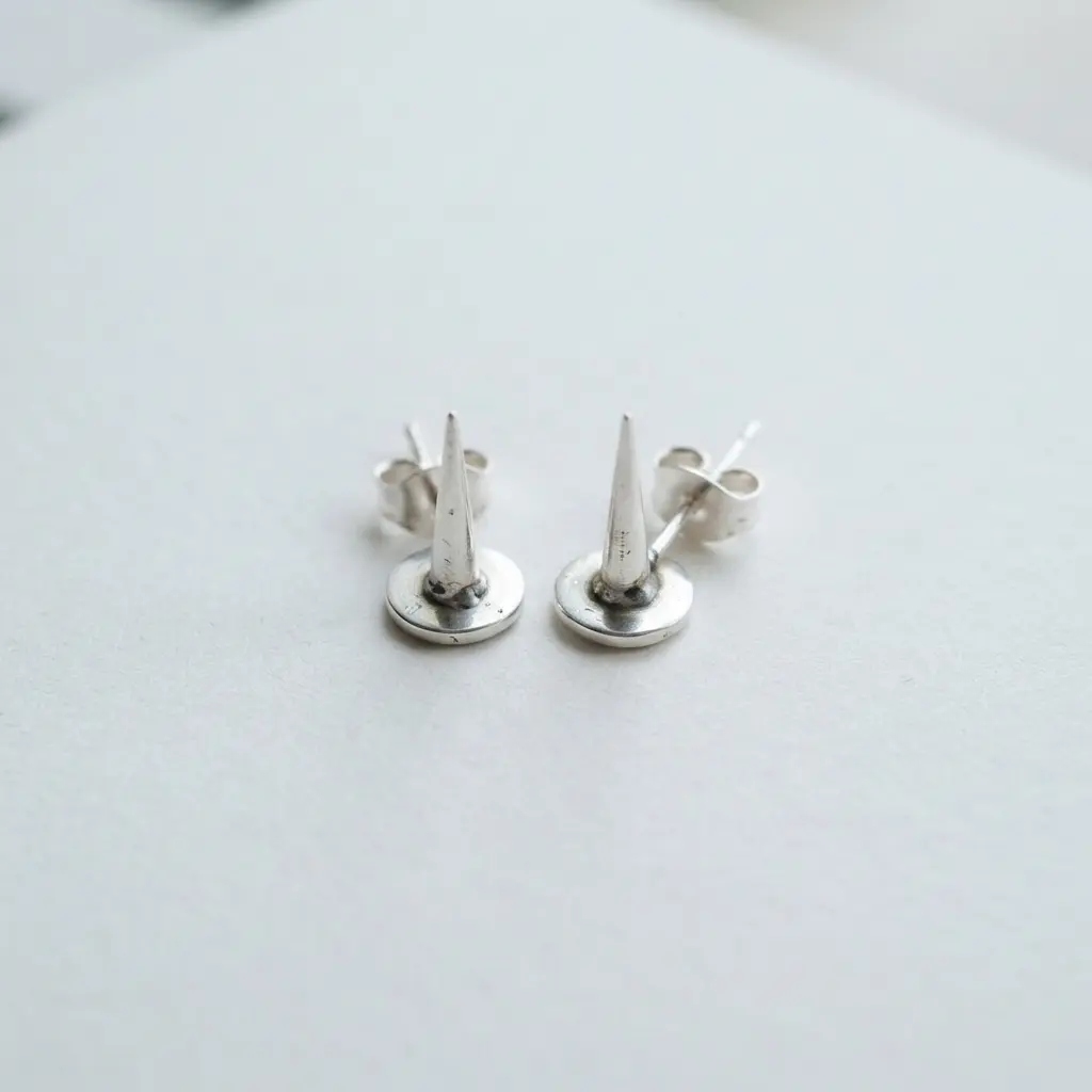 Close-up of small, polished silver spike studs on earring posts against a dark background.