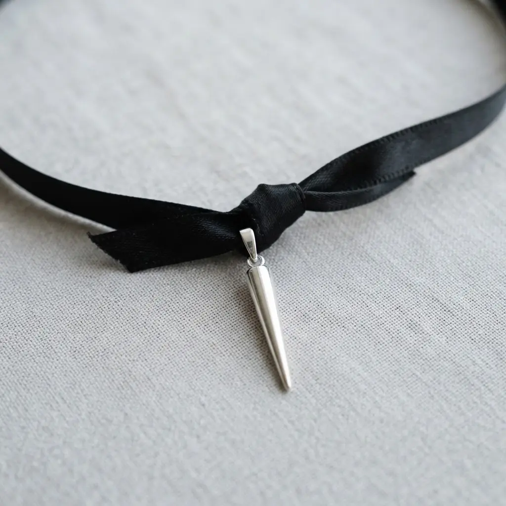 A minimalist necklace with a delicate black satin ribbon and a lone silver spike charm.