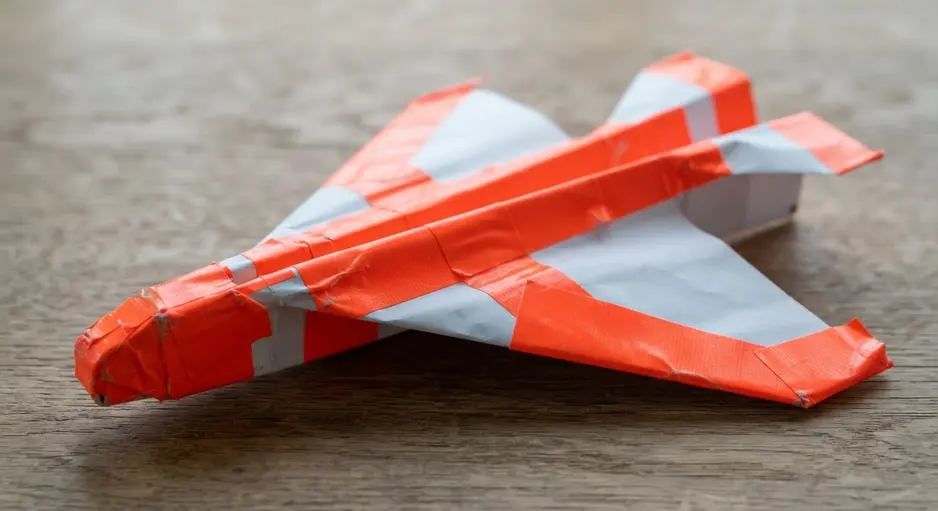 A white paper airplane with its wings and body reinforced and decorated with strips of neon orange duct tape.