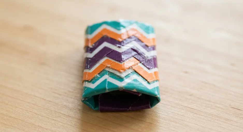 A wooden pencil topped with a small, three-dimensional shape crafted from layered strips of chevron-patterned duct tape.