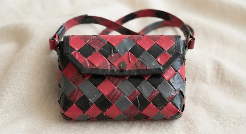 A miniature purse with a flap closure, constructed from a sheet of duct tape woven in a red and black plaid pattern.