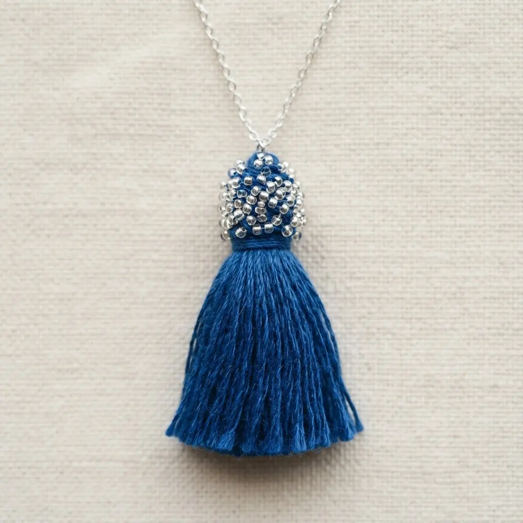 A short necklace with a blue floss tassel featuring a detailed top section adorned with tiny silver seed beads.
