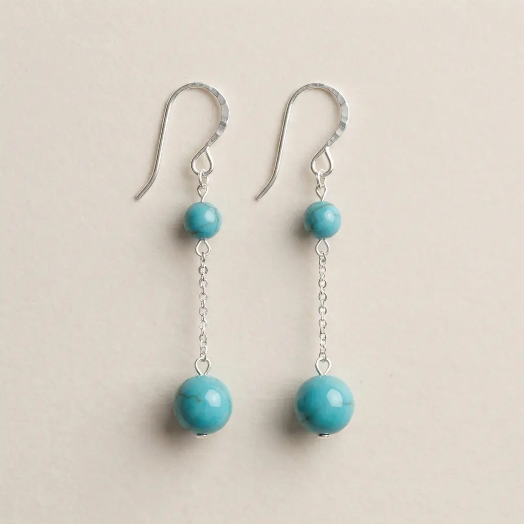 A pair of dangle earrings featuring two round turquoise beads connected by a tiny silver chain.