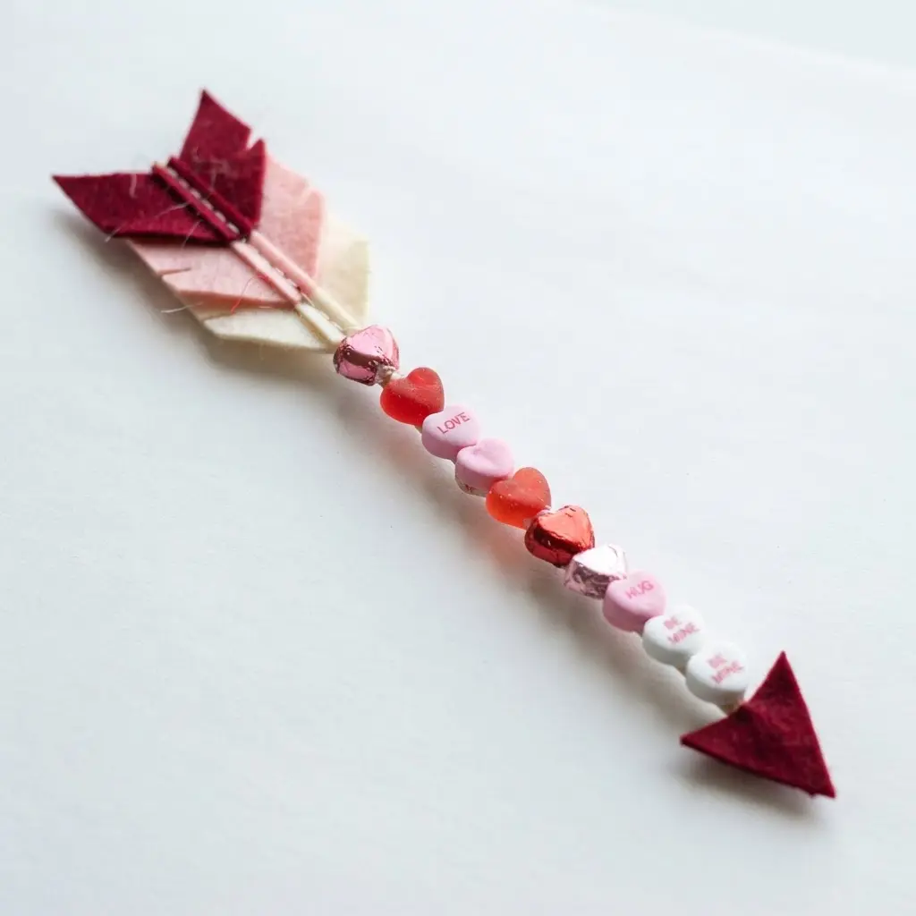 A decorative arrow where the shaft is a line of glued candy hearts, finished with soft red felt feathers at the end.