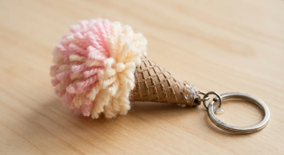A miniature pink and white yarn pom pom cone on a metal keychain ring.