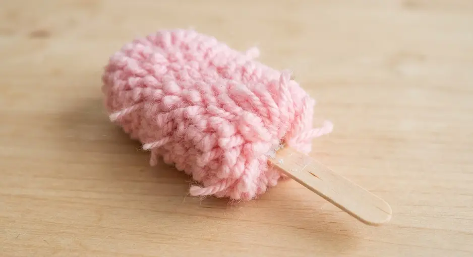 A small, rectangular pink pom pom on a craft stick, resembling a classic ice cream bar.