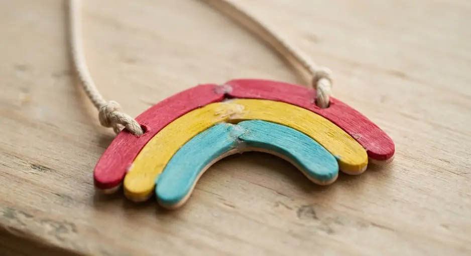 A colorful rainbow arc pendant constructed from painted mini popsicle sticks on a cord.