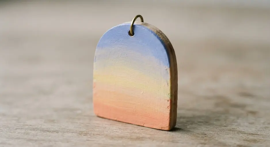 An arched wood pendant showing a gentle gradient from pink to yellow to light blue.