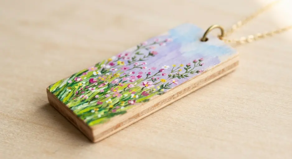 A miniature painted scene of flowers and grass on a small wooden pendant.