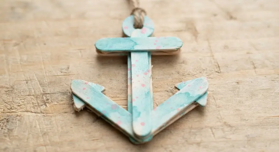 An anchor-shaped charm made from mini sticks with a soft blue and pink speckled paint effect.
