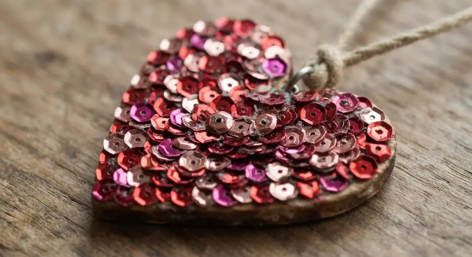 A wooden heart pendant densely covered with shimmering red and pink sequins.