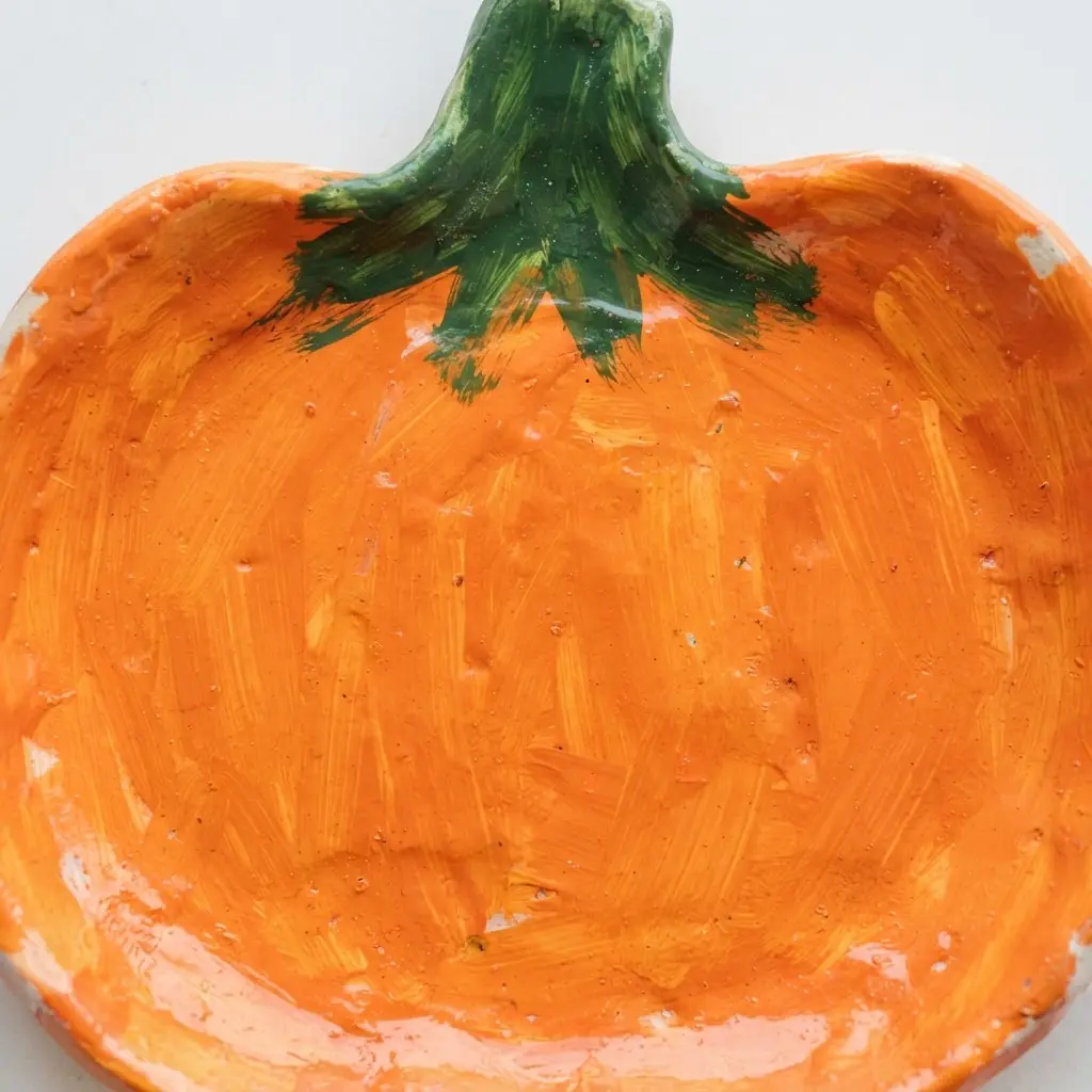 An easy pottery painting idea for fall, a pumpkin-shaped dish is painted orange.