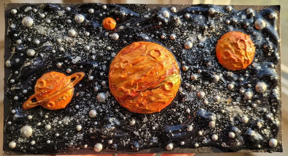 A space scene with puffy paint planets, stars, and a rocket on a black cardstock background.