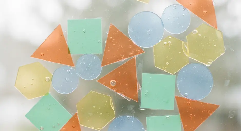 A sunlit window decorated with translucent orange circles and green triangles made of static-cling vinyl.
