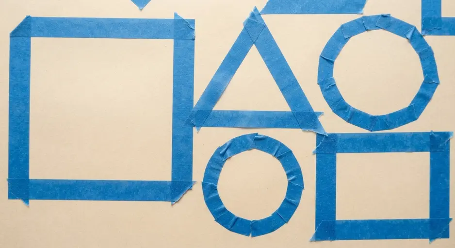 A child stepping inside a large triangle outline made from blue painter's tape on a light-colored floor.