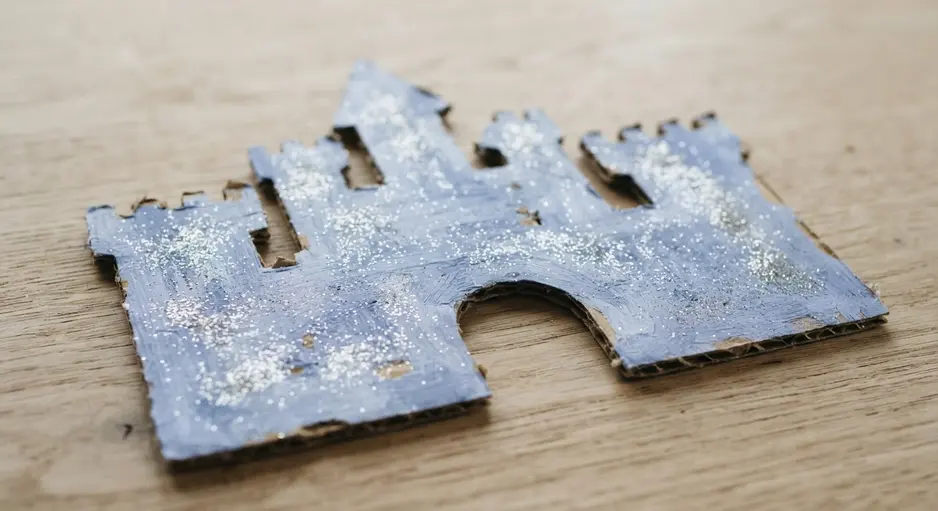 A simple castle silhouette cut from cardboard, painted blue, and decorated with silver glitter.