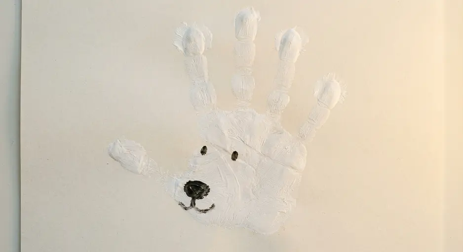 A polar bear face created by painting a child's hand white and pressing it onto blue paper.